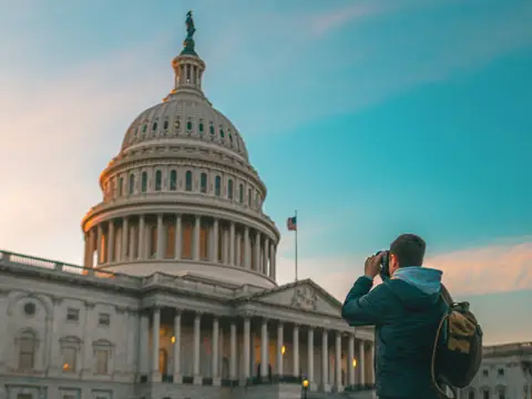 A man with a backpack photographs the US Capitol under a clear sky