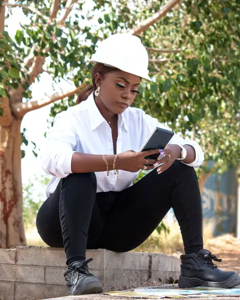 An engineer in a white hard hat checks her phone at a work site