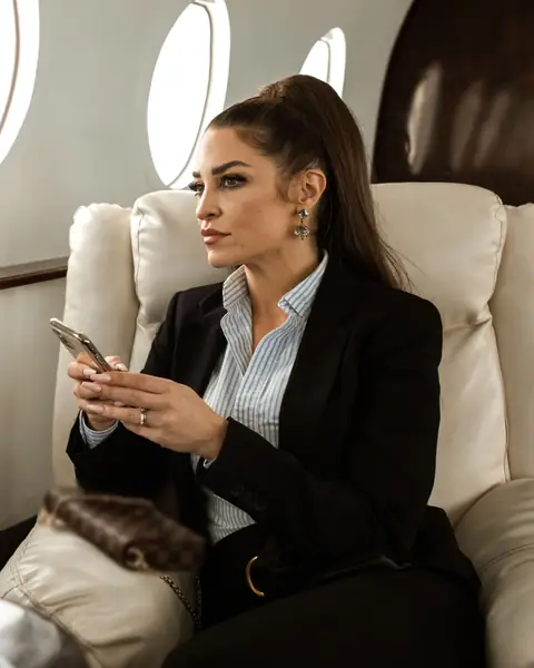 A woman in a dark suit holds her phone in the cabin of a private jet